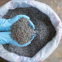 someone holding fertilizer in their hands, over a large bag of fertilizer